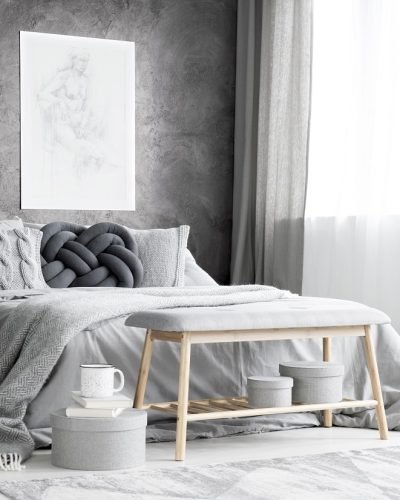 Spacious bedroom with armchair, knot cushion on the bed and two posters hanging on textured wall