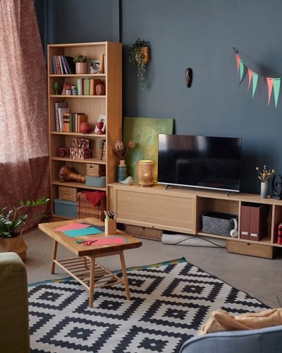 Living room decorated for Kwanzaa celebration featuring colorful pennant banners, traditional unity cup, bookshelves, television, and stationery for crafting on table
