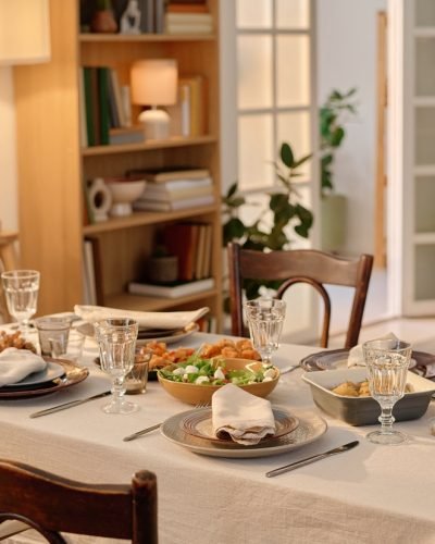 Medium close up of table covered with cotton tablecloth and served with Greek salad, baked potatoes with olive oil mixed herbes de Provence and snacks