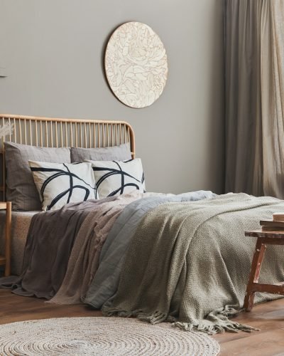 Wooden bed in stylish neutral bedroom interior with design furniture, decoration, carpet, bench, dried flowers in vase, bed sheets, blanket, pillows and elegant personal accessories in home decor.